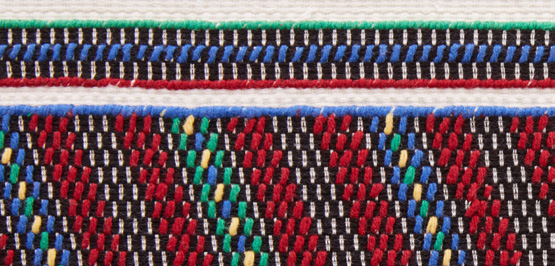 Geometrikus mintájú, élénk színű (fekete, vörös, kék, fehér, zöld) szövött textil részlete, vízszintes csíkokkal és kis virágmotívumokkal.